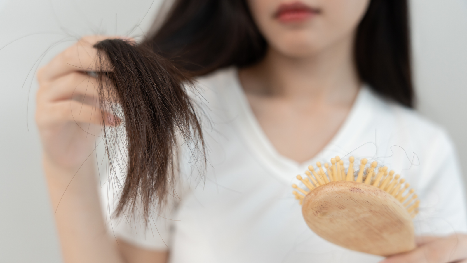 Donna che osserva capelli caduti sulla spazzola, simbolo di caduta dei capelli stagionale e stress autunnale.