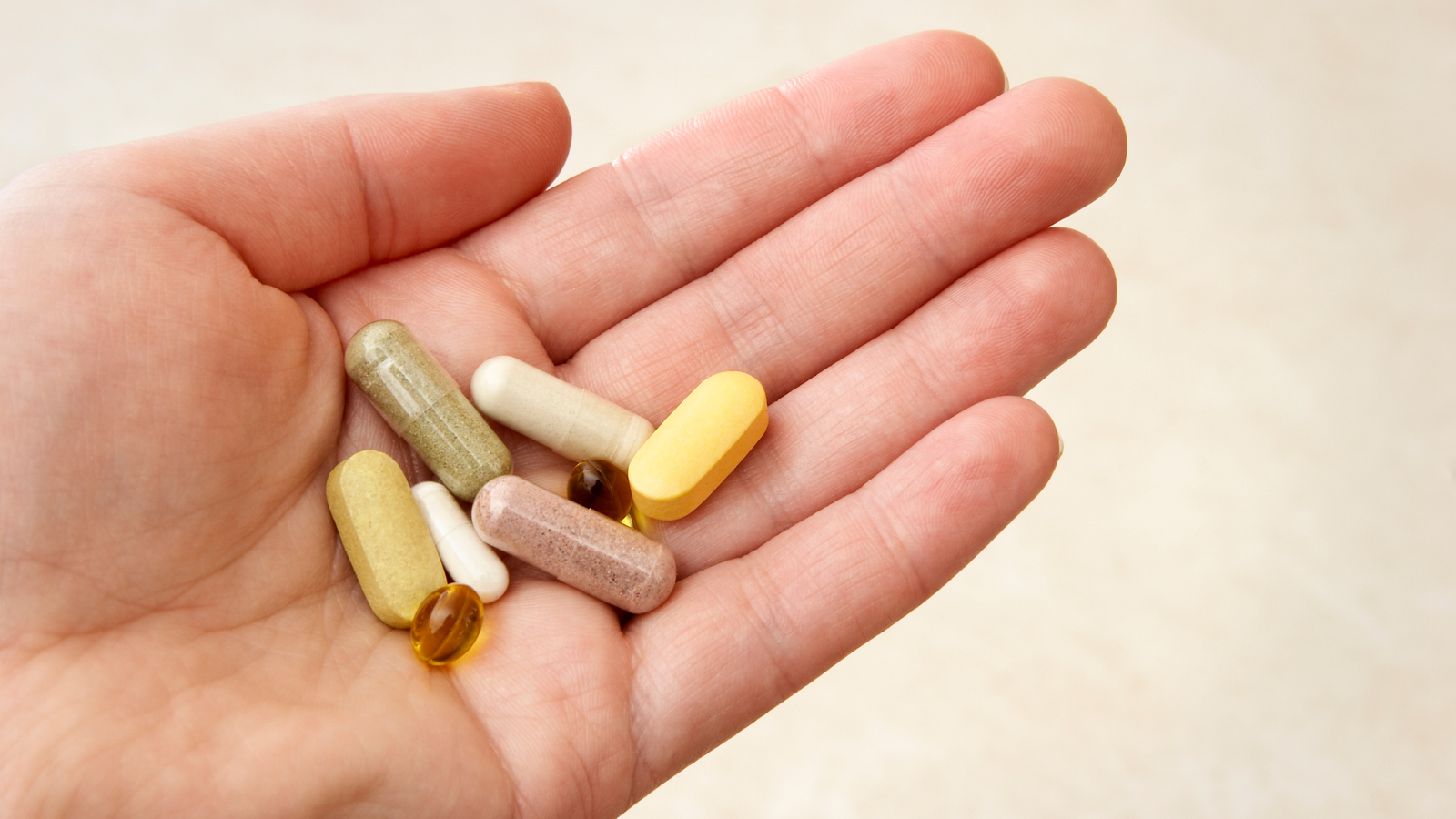 Mano che tiene capsule e compresse multivitaminiche di diversi colori, simbolo degli integratori per rafforzare le difese immunitarie in autunno.
