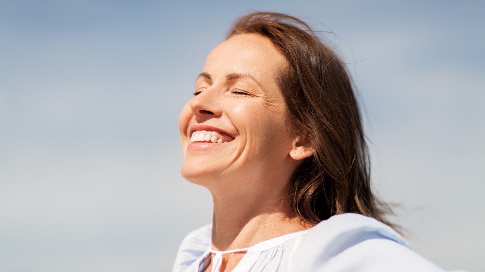 Donna che sorride al sole con gli occhi chiusi, simbolo della produzione naturale di vitamina D e del benessere legato alla luce solare.